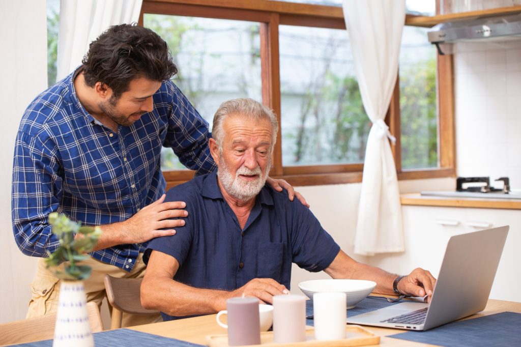 Edmonton dementia care in home, good mentor healthy smart old man using laptop computer stay at young man.